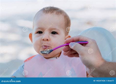 Dad Feeds The Baby With A Spoon Of Porridge Outdoors Stock Photo