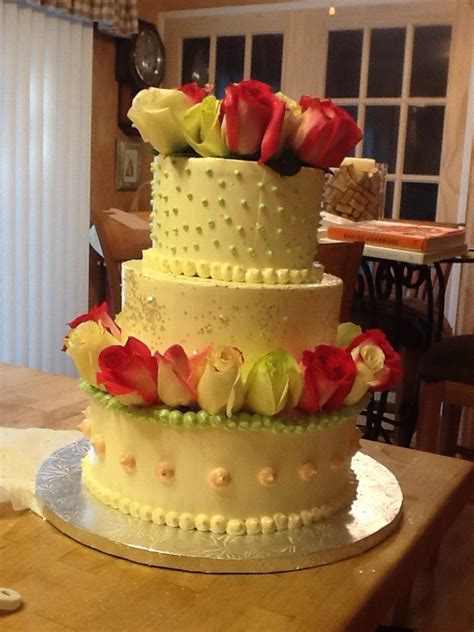 A Three Tiered Cake With Flowers On The Top Is Sitting On A Wooden Table