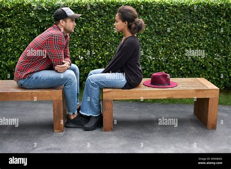 Thoughtful Interracial Couple Sit On Wooden Benches On The Green Bushes