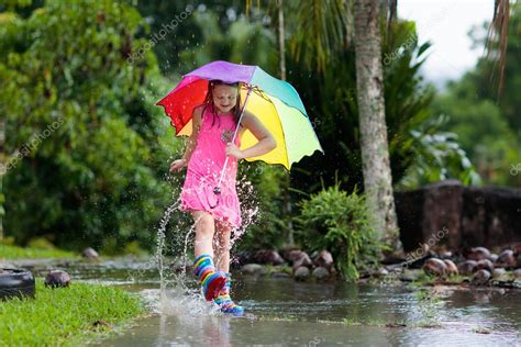 El chico jugando bajo la lluvia Los niños con paraguas y botas de lluvia juegan al aire libre