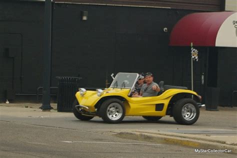 A Man Driving A Yellow Sports Car Down The Street