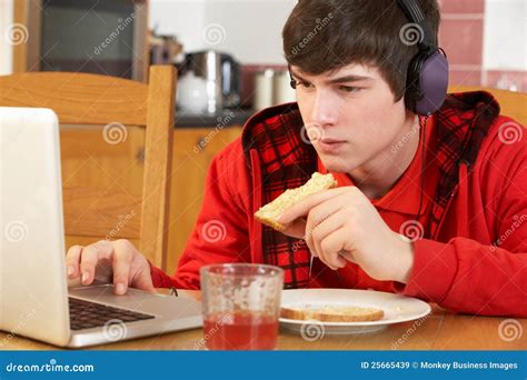 Adolescente Que Usa La Computadora Portátil Mientras Que Come El Desayuno Imagen De Archivo