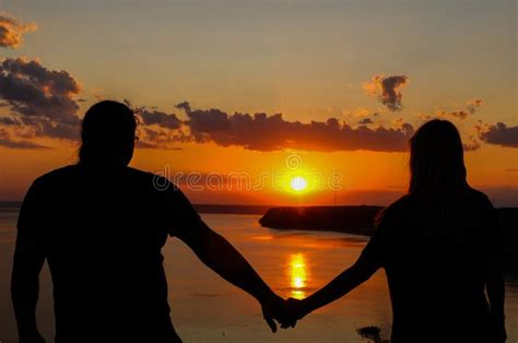Silhouette Of Romantic Couple Holding Hands On The Beach And Looking At Sunset Over The Sea