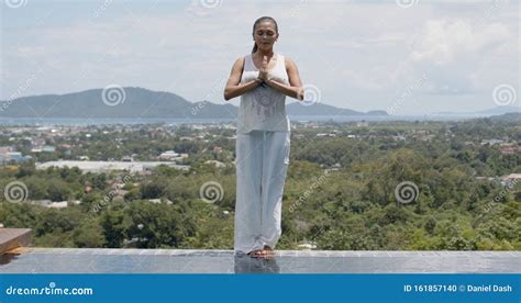 Woman Meditating While Standing Poolside Against Tropical Coast Stock