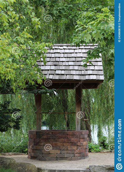 A Brick Wishing Well With A Wood Shingled Roof Surrounded By A Weeping