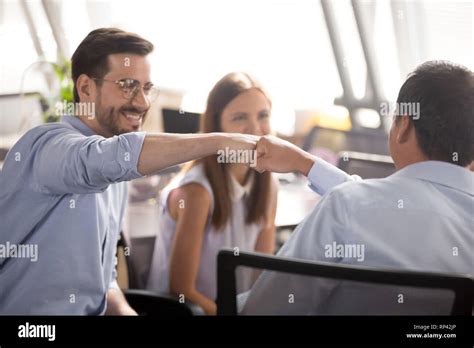 Millennial Cheerful Positive Male Colleagues Sitting On Chairs In Coworking Area Fist Bumping