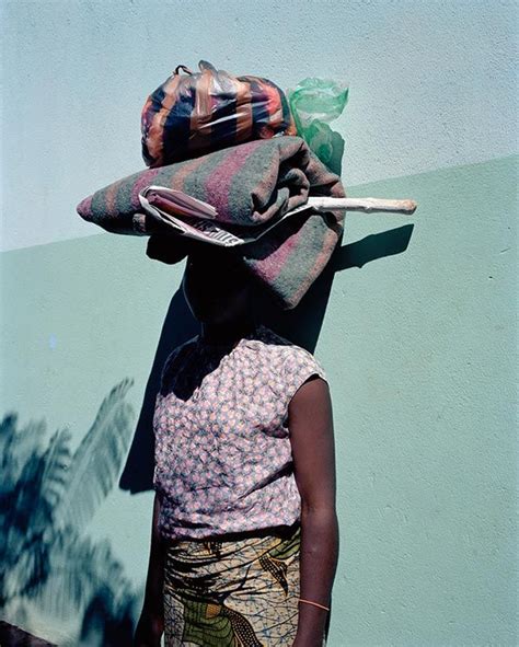 A Woman Standing In Front Of A Wall With A Hat On Her Head And A Bag