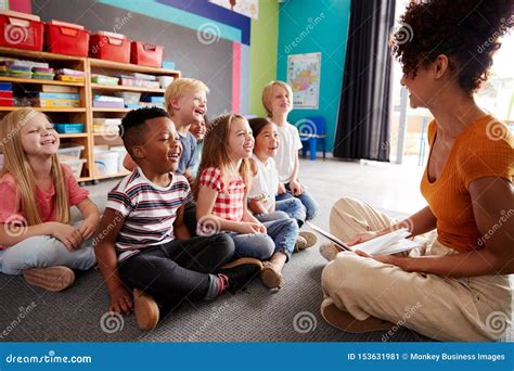 Group Of Elementary School Pupils Sitting On Floor Listening To Female