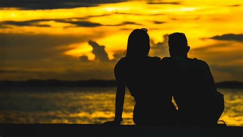 Silhouette Of Couple Sitting On Seashore During Sunset · Free Stock Photo