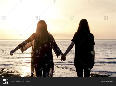 Silhouette Of Two Young Women Watching The Sunset While Holding Hands
