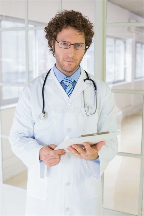 Serious Male Doctor Standing With Clipboard In Hospital Stock Image