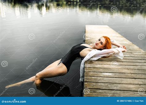 Slim Redhead Girl With Body In A White Shirt On A Pier By The Lake