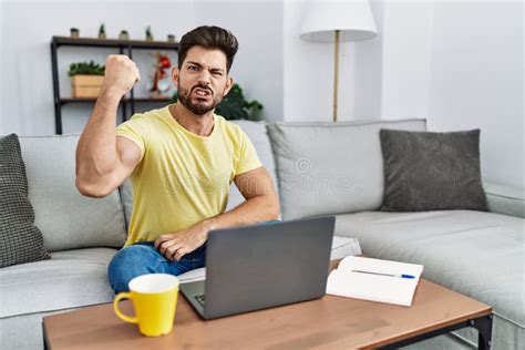 Young Man With Beard Using Laptop At Home Angry And Mad Raising Fist