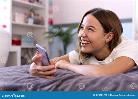 Smiling Teenage Girl Lying On Bed At Home Looking At Mobile Phone Stock