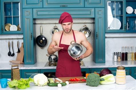 Premium Photo Man Chef In Red Hat Apron On Bare Torso Point At Saucepan At Kitchen Table