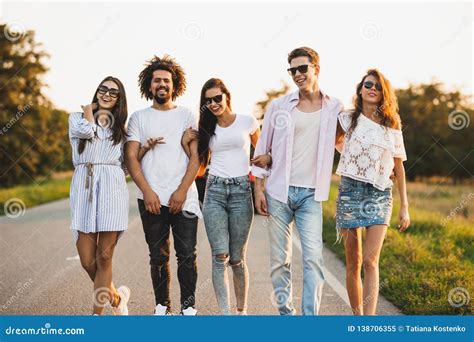 Young Stylish Two Guys And Three Girls Are Holding Hands And Walking On
