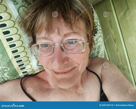 A Shaggy Funny Middle Aged Woman In Glasses Takes A Selfie On Her Smartphone In The Bed In