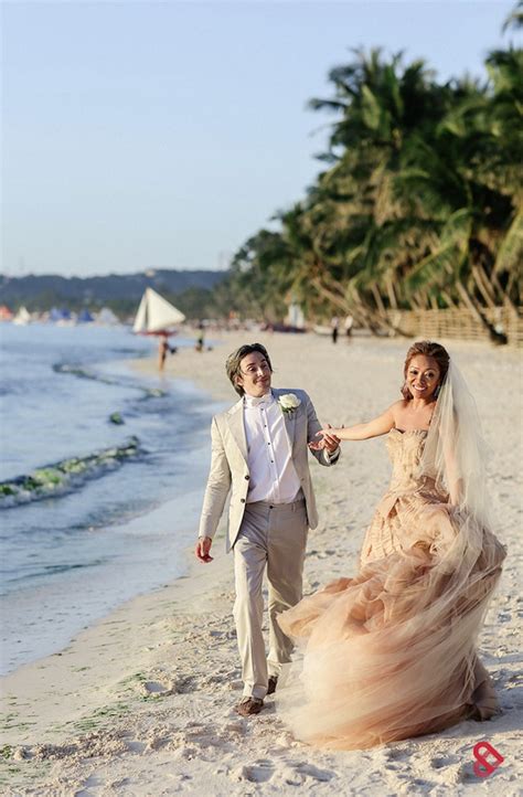 A Bride And Groom Are Walking On The Beach Holding Hands While Dressed