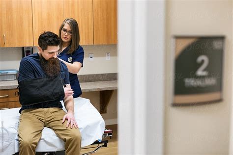 Clinic Nurse Helps Put Sling On Patient By Stocksy Contributor Sean Locke Stocksy