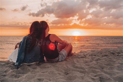 Couple Of Lesbian Girls Sitting On The Beach And Watching And Enjoying A Beautiful Sunset
