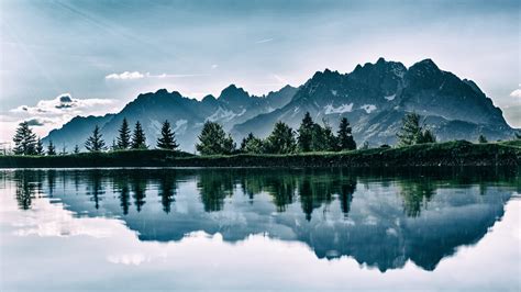 Landscape View Of Green Trees Snow Covered Mountains Reflection On Calm