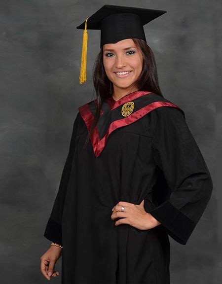 A Woman Wearing A Graduation Cap And Gown Poses For A Photo In Front Of
