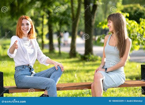 Two Happy Girls Friends Sitting On A Bench Outdoors In Summer Park Chatting Happily Having Fun