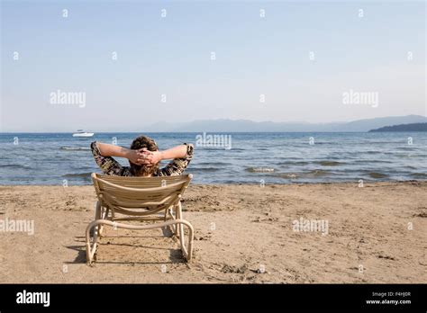 entspannte frau sitzt auf einem stuhl am strand mit ihren händen hinter dem kopf verschränkt