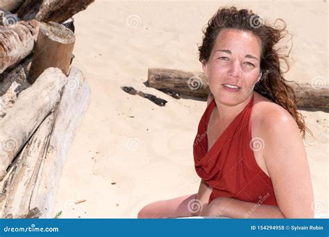 Donna Sorridente In Vestito Rosso Che Si Siede Sulla Spiaggia Di Sabbia Nel Giorno Di Estate