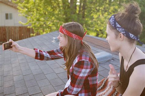 Teen Girls Take Selfies With Phone While Sitting On Roof Top By Tana