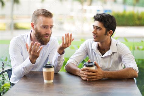 Two Male Friends Drinking Coffee And Talking In Outdoor Cafe People Sitting At Table With