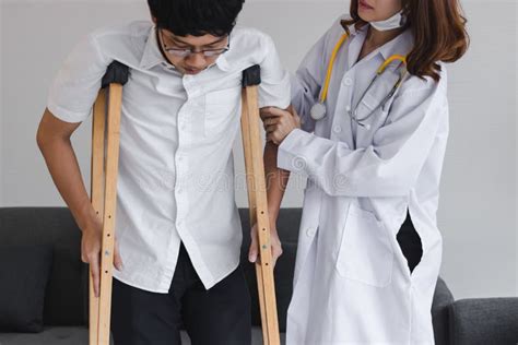 Physical Female Doctor Helping Patient With Crutches In Hospital Office