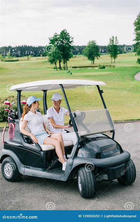 Female Golfers In Caps Looking At Each Other In Golf Cart Stock Photo
