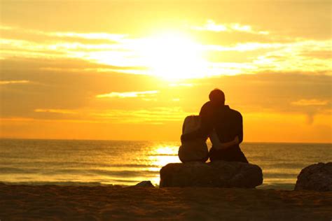 Loving Embraced Couple Sitting And Watching Sunset On Beach Stock
