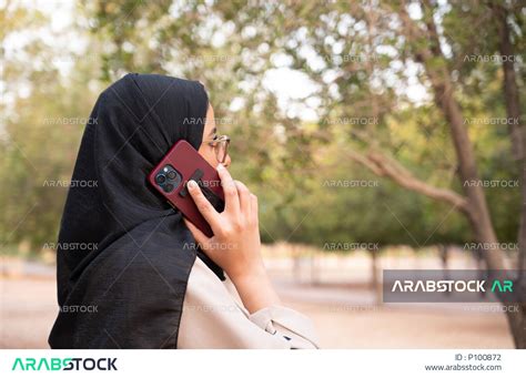 شابة عربية خليجية سعودية محجبة تقوم بالدردشة عبر الجوال و تقضي أوقات ممتعة في إحدى الحدائق