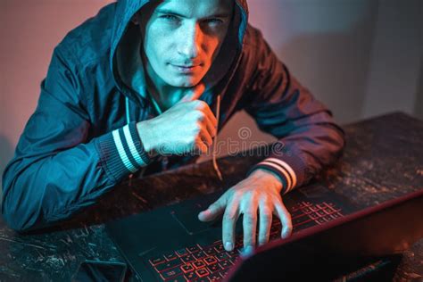 Hooded Hacker Is Typing On A Laptop Keyboard In A Dark Room Under A