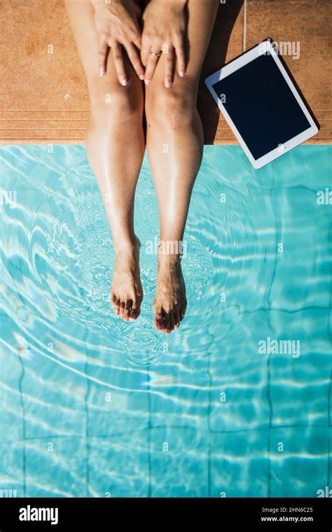 unrecognizable woman next to a tablet at the edge of a turquoise pool getting her feet wet stock