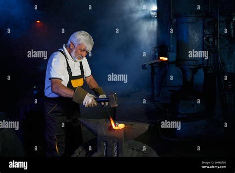 Aged Caucasian Blacksmith Wearing Safety Apron And Gloves Forging Steel