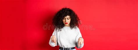 Worried Young Woman With Curly Hairstyle Looking Down And Pointing At