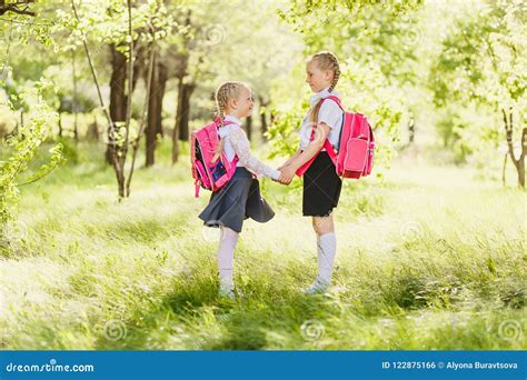 Zwei Kleine Schulmädchen In Der Schuluniform Stehen Mit Rucksäcken Und