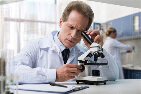 Concentrated Scientist In White Coat Looking Into The Microscope In