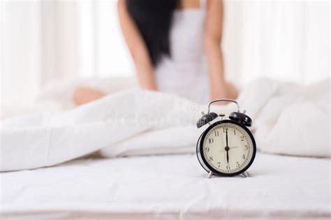 Close Up Of Alarm Clock At 6 O`clock In The Morning And Blurred Woman Waking Up In Her Bedroom
