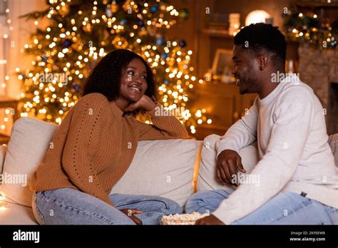Smiling Young African American Husband And Wife Talking Sit On Sofa With Popcorn In Living Room
