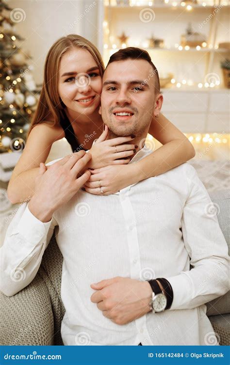 Couple In Love Kisses And Hugs On The Sofa Near The Christmas Tree Lights New Year`s Night