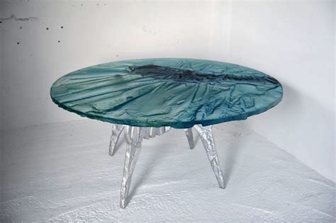 A Glass Table Sitting On Top Of A Snow Covered Ground Next To A White Wall