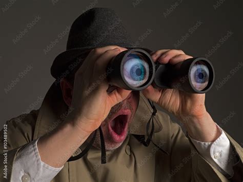 Photograph Of A Man In Trench Coat And Hat Looking Through Binoculars With Huge Cartoonish Eyes