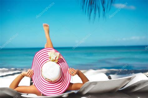 Beautiful Woman Model Sunbathing On The Beach Chair In White Bikini In Colorful Sunhat Behind