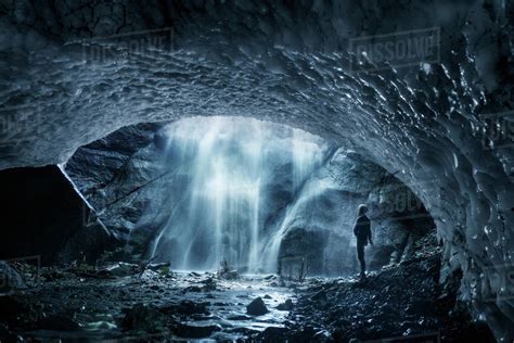 Side View Of Man Looking At Waterfall While Standing In Ice Cave