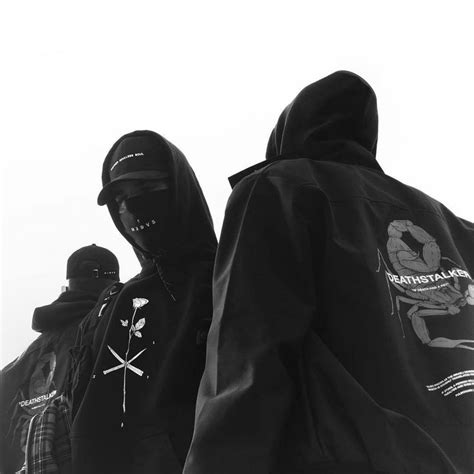Two People Wearing Hoods And Jackets Standing Next To Each Other In