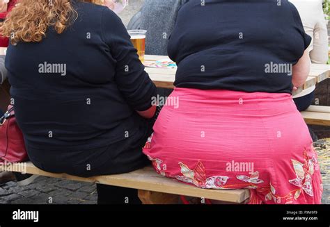 Rear View Of Two Obese Women Sitting On A Bench Drinking Outside At The
